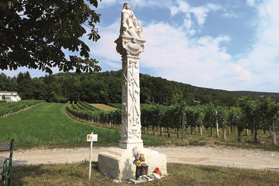 Steinerner Bildstock auf einer Säule vor Weingärten.